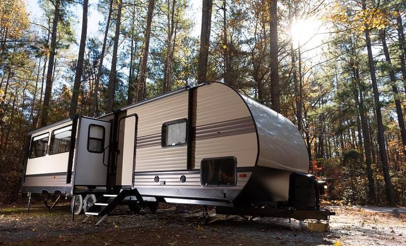 A large RV with a slide-out room and camper seals sits in a wooded area