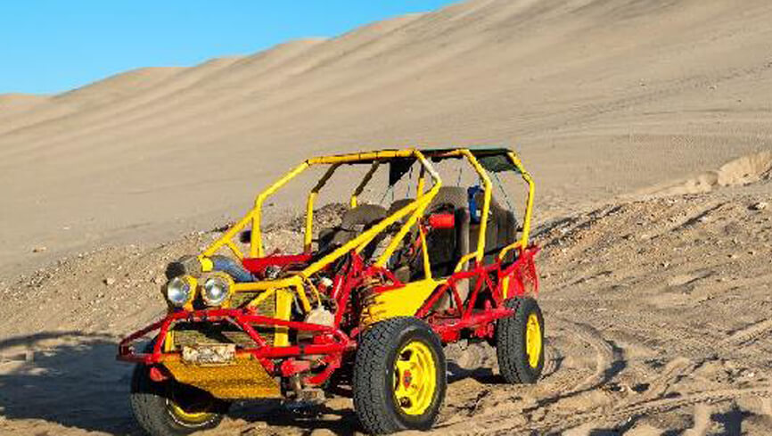 A yellow and red dune buggy or sand car on a large dune